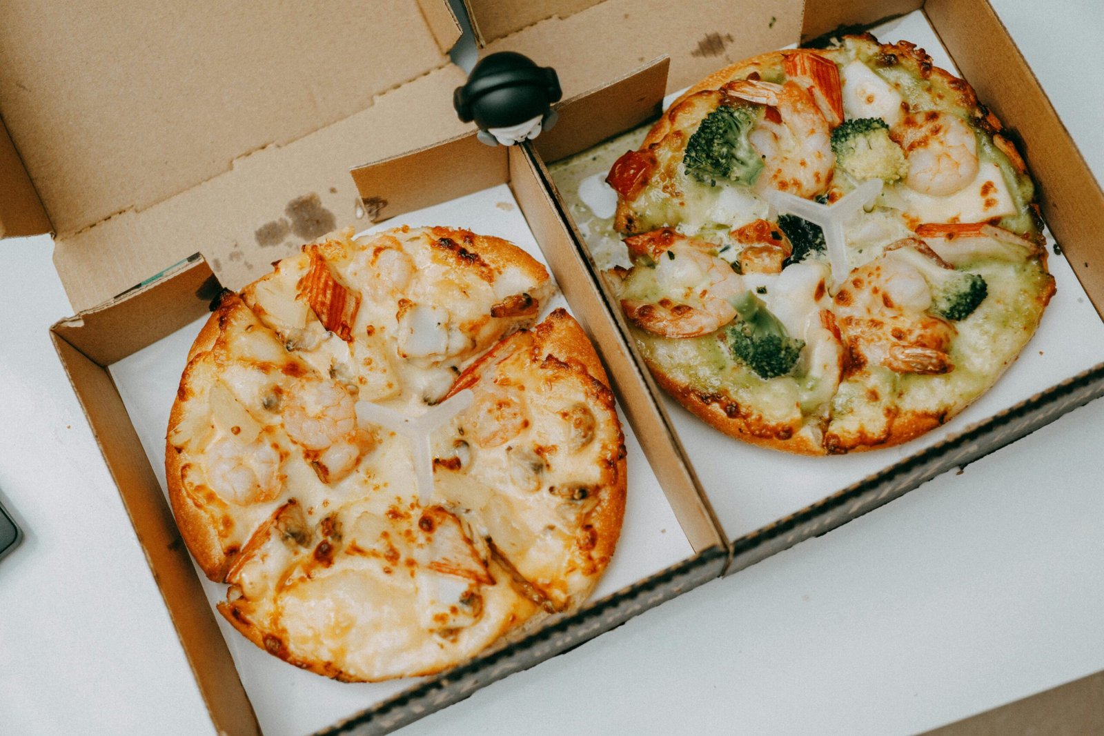 Two tasty shrimp pizzas with vegetables in delivery boxes on a table.