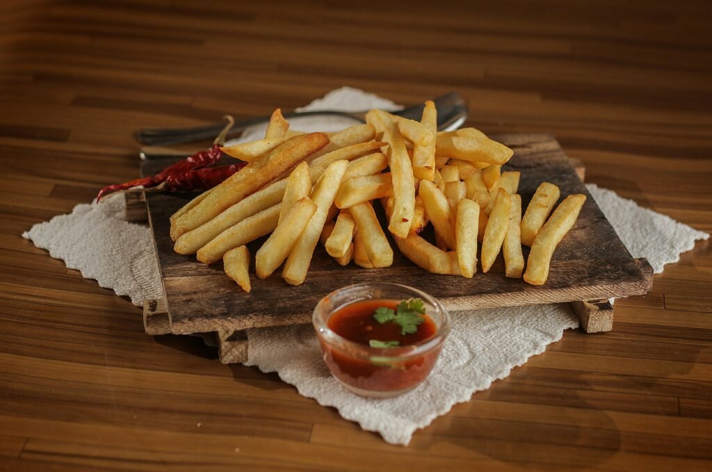 Golden French fries served on a rustic wooden board with spicy ketchup and chili pepper garnish, perfect for fast food lovers.