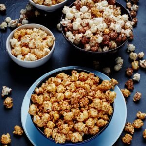 Top view of assorted flavored popcorn in bowls, showcasing sweet and salty varieties on a dark surface.