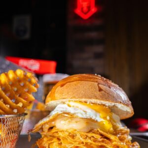 Mouth-watering chicken burger with fried egg and waffle fries in a vibrant restaurant setting.