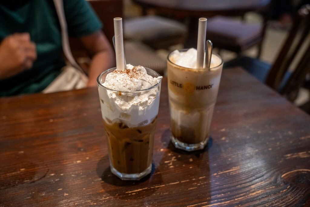 A close-up of two iced coffee drinks with whipped cream at Little Hanoi, perfect for a refreshing break.