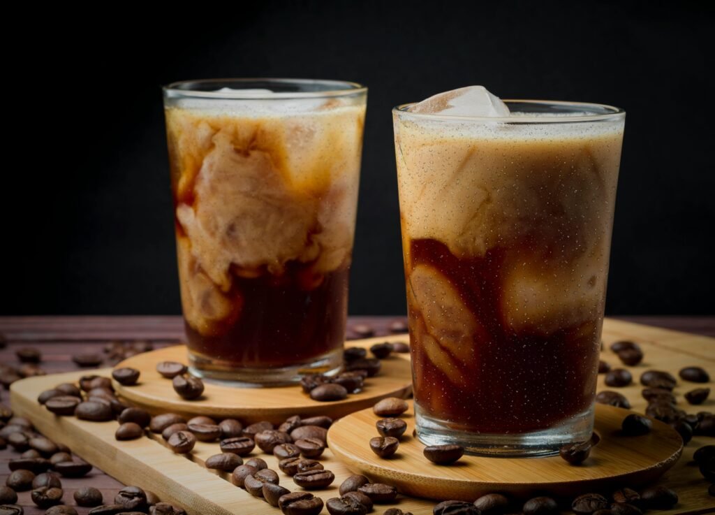 Delicious iced coffee with swirling cream served in glass cups surrounded by coffee beans.