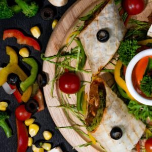 A vibrant flat lay of a vegetable wrap surrounded by fresh ingredients on a rustic wooden board.
