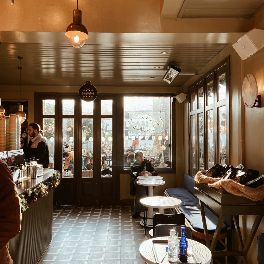 Warm and inviting café interior with wooden furniture, large windows, and soft lighting.